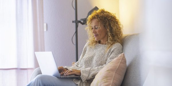 Relaxed and happy adult attractive woman working at home with laptop computer comfortably sitting on the sofa - concept of modern people and home work activity  - independent lady use notebook online to surf the web
